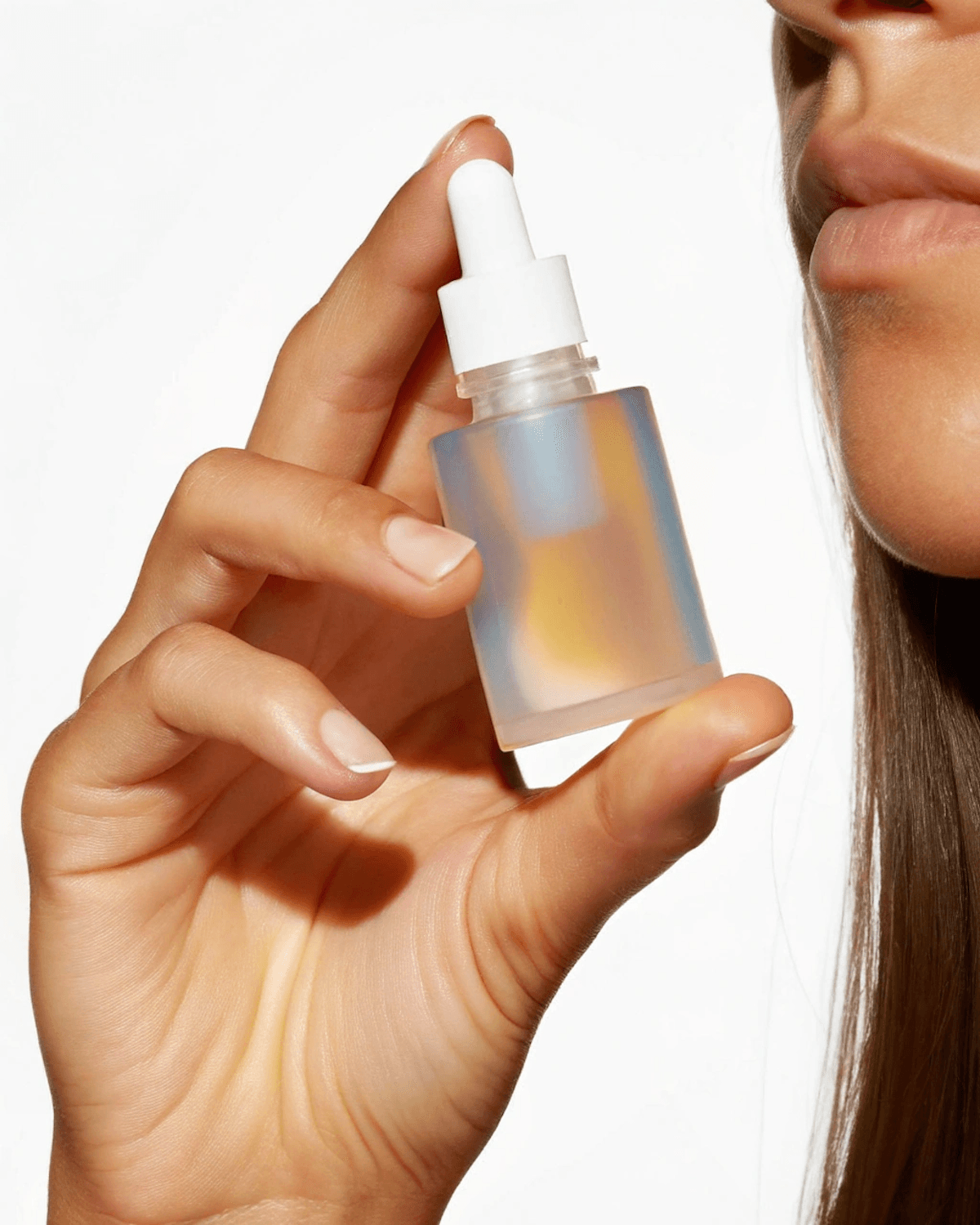 Hand holding a frosted, iridescent hair oil dropper bottle